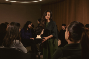 An educator demonstrating technique to a seated room of beauty professionals.