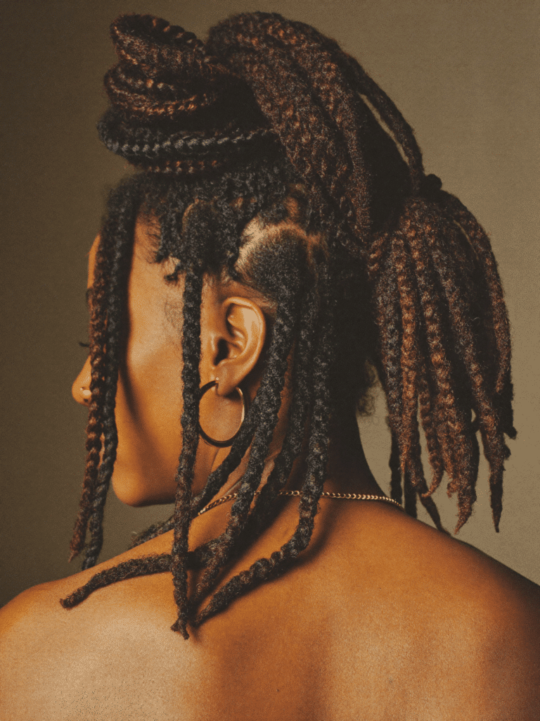 Mature locs styled into a high sculpted updo under warm studio light.