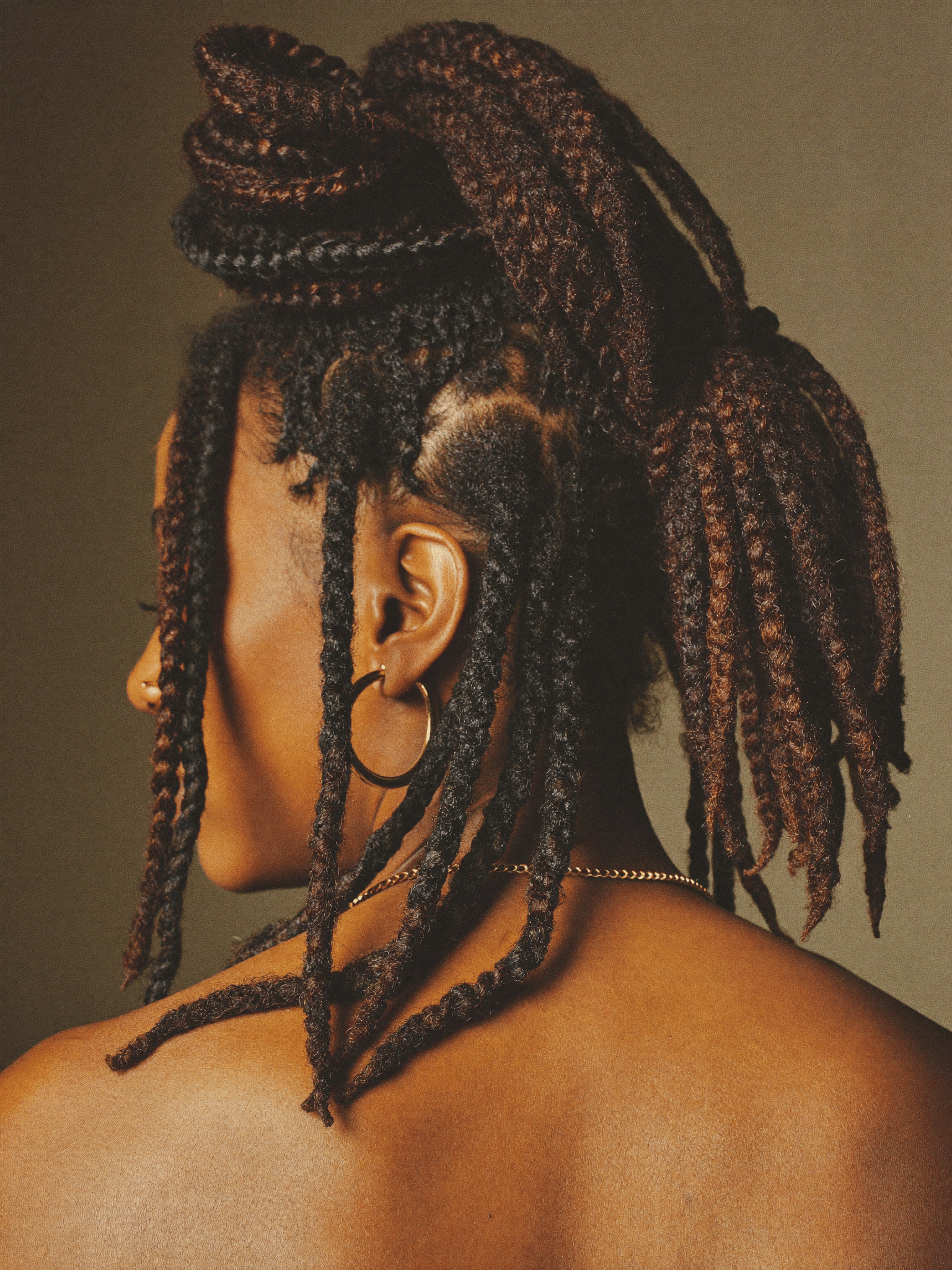Mature locs styled into a high sculpted updo under warm studio light.