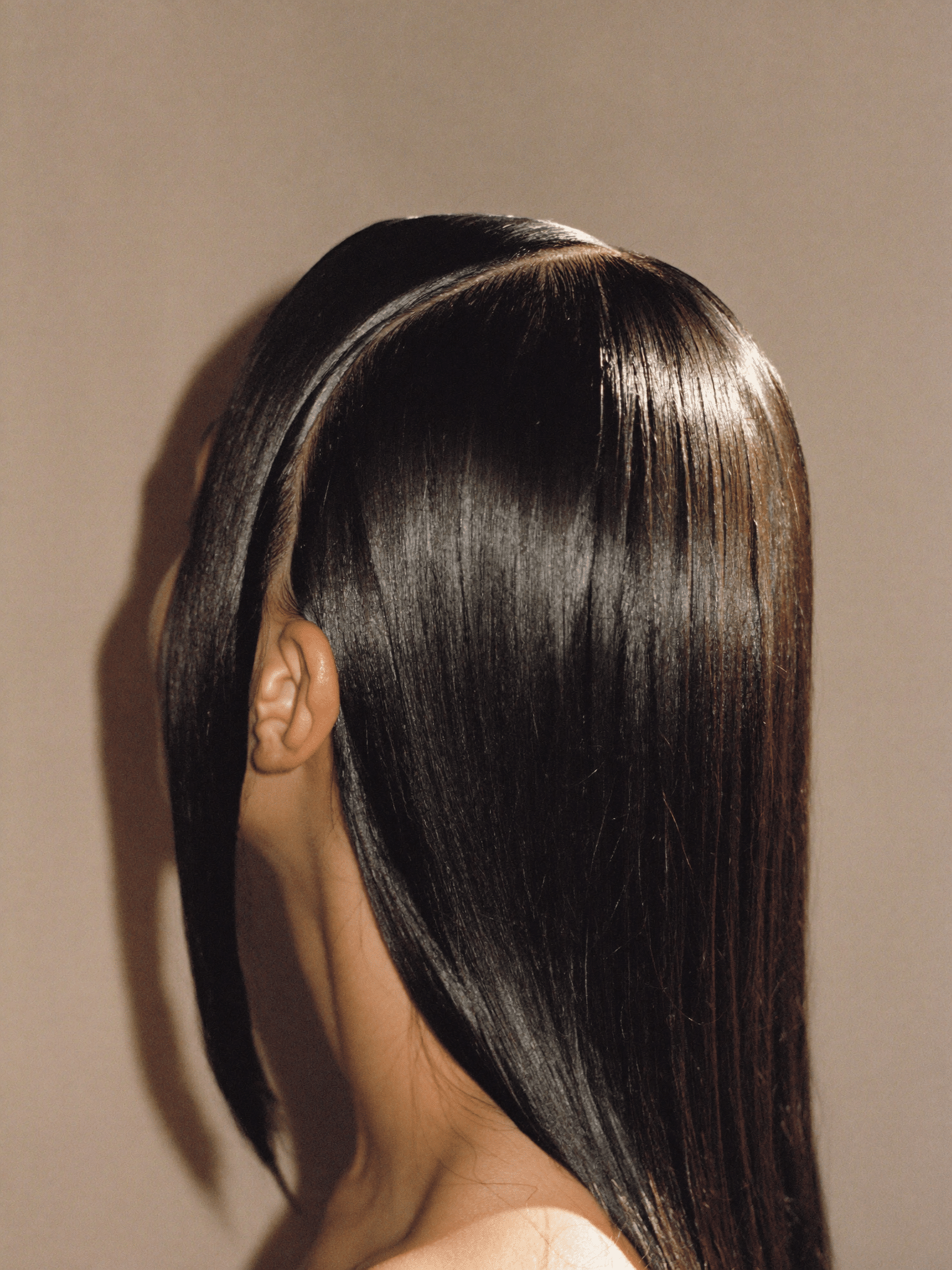 A glossy silk press with a sharp centre part, photographed in profile under warm studio light.