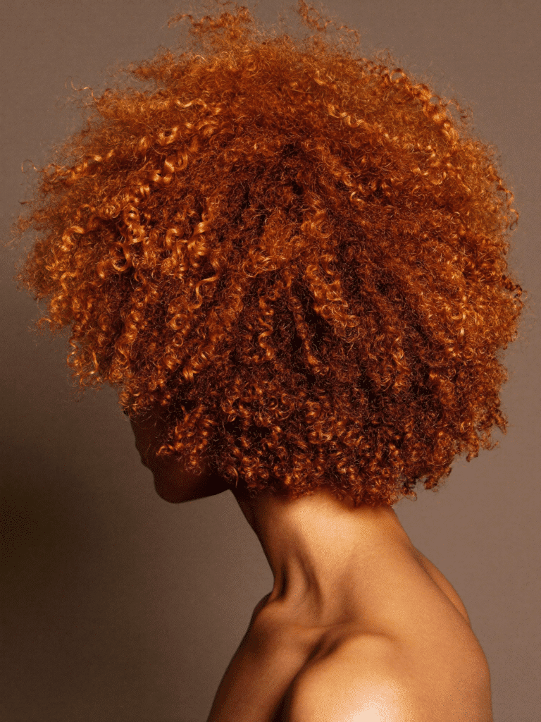 Vivid copper balayage on textured curly hair showing dimensional colour.