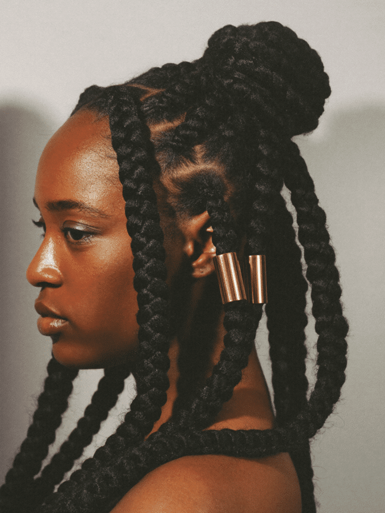 Long jumbo knotless box braids styled in a half-up bun with gold cuffs.